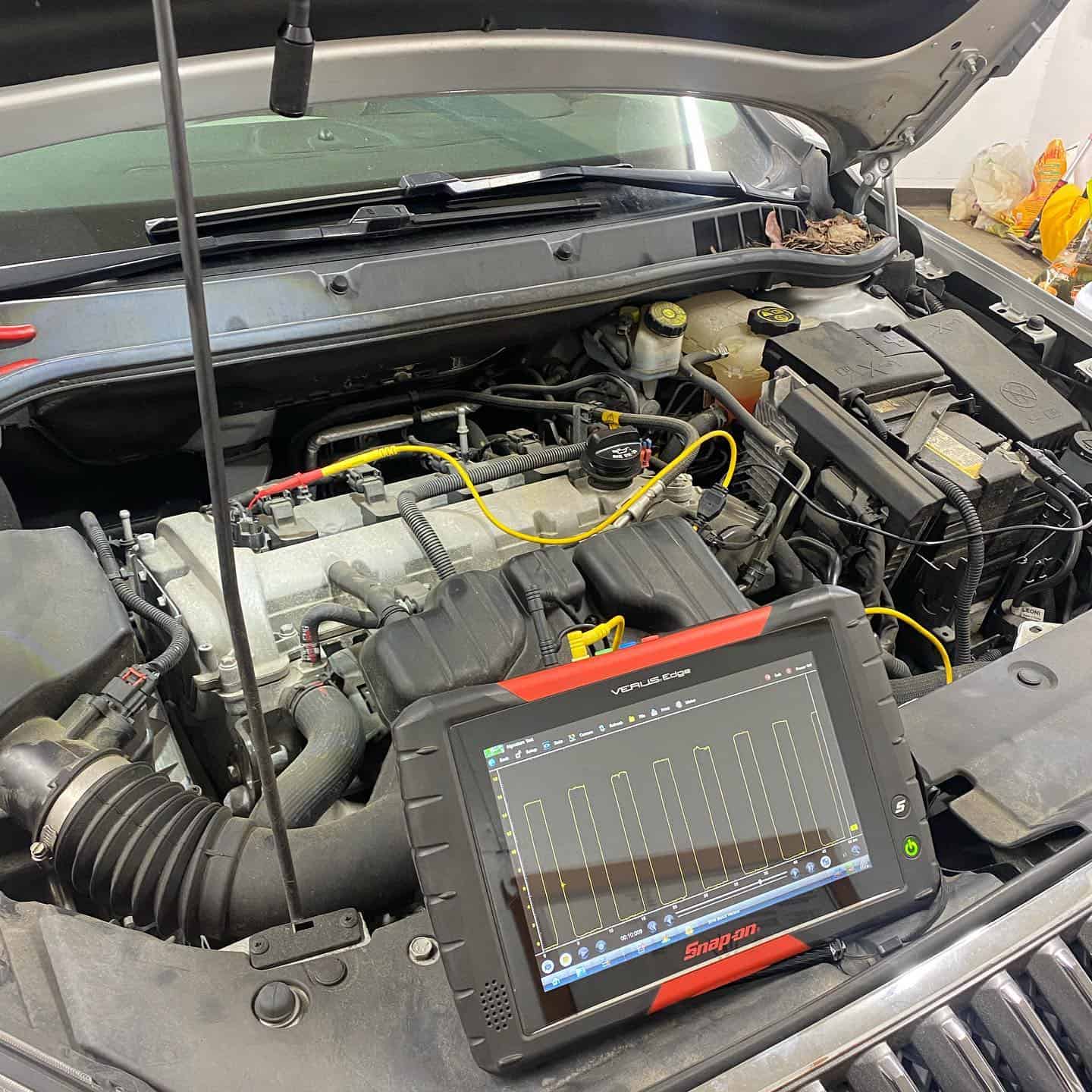 Image of a scanner diagnostics tool and an open hood of a car. Concept image of vehicle diagnostics and digital vehicle inspection at Enright Automotive.