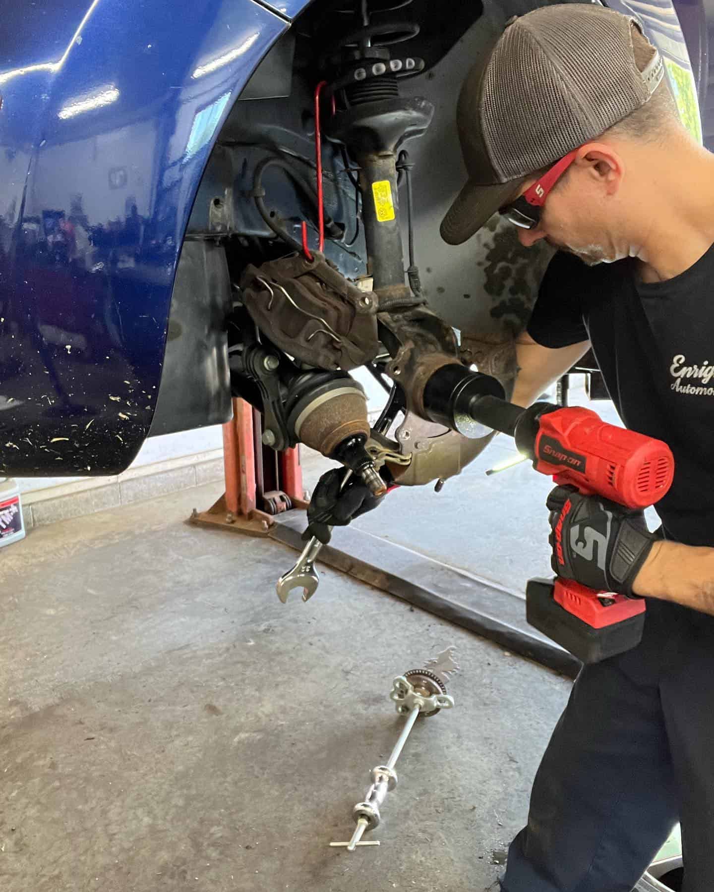 Image of Chris Enright holding a high impact torque wrench tool and using other tools in fixing a lifted blue car. Concept image of Japanese auto repair at Enright Automotive.