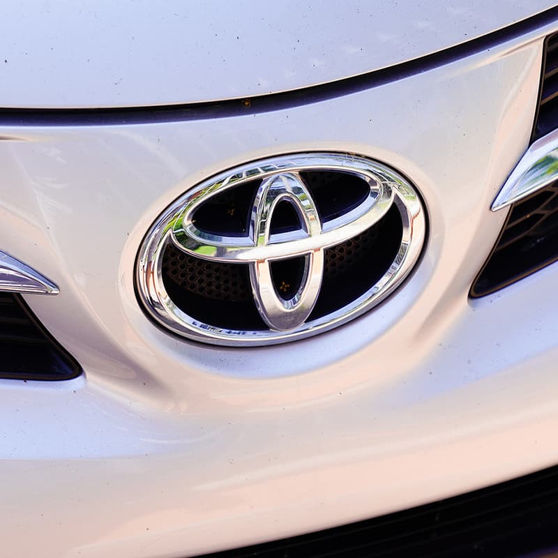 Closeup image of a white Toyota car with focus on the Toyota logo. Concept image of vehicle we service for auto repair and maintenance at Enright Automotive.