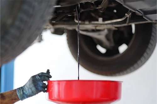Preventative Maintenance & Why It's Important | Enright Automotive in Alexandria, OH. Image of an auto mechanic flushing and changing oil as part of preventative maintenance.