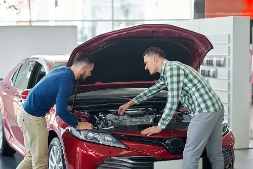 Buying or Selling a Used Car? Maintenance Matters More Than Mileage | Enright Automotive in Alexandria, OH. Image of two male friends in casual clothes, with guy on the right helping the guy on the left check the condition of a used red car before purchasing..