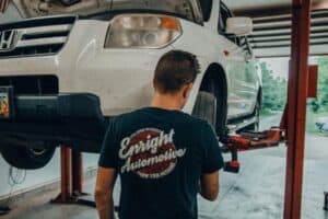 Engine Maintenance in Alexandria and Pataskala, OH with Enright Automotive. Image of a white Honda car lifted for inspection by a mechanic at Enright Automotive.