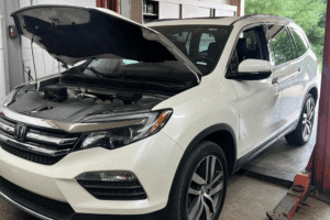 Honda aftermarket parts, auto repair in Alexandria, OH at Enright Automotive. Image of a white Honda SUV inside the repair shop with the hood open, showing the engine bay during inspection and service.